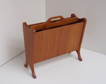 May include: A wooden magazine rack with a handle on the top. The rack is made of light brown wood and has a simple design.