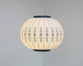 May include: A white, round, hanging lampshade with a black trim and a floral pattern. The lampshade is made of a pleated material.