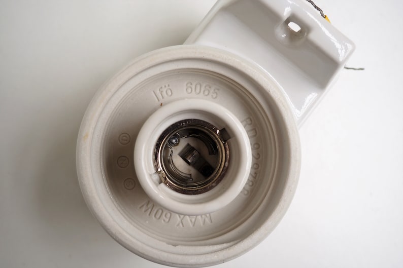 May include: White ceramic light fixture with a metal light bulb socket. The fixture has the text "If&ouml; 6065" and "MAX 60W" printed on it.