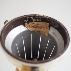 May include: Close-up of the inside of a white metal lampshade with a brown metal rim. A label with the text "Vitrika Dekorations pendel" is attached to the rim.