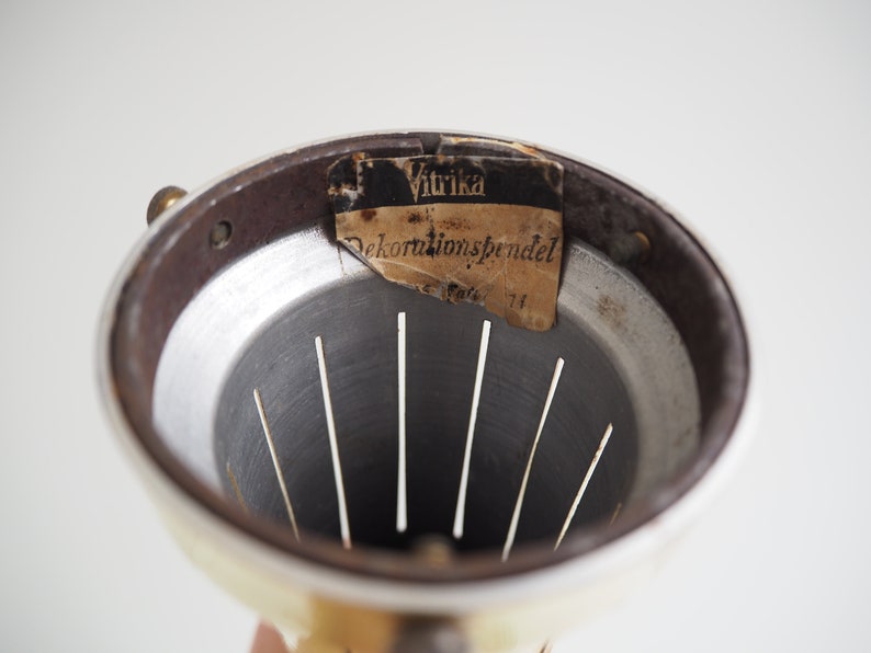 May include: Close-up of the inside of a white metal lampshade with a brown metal rim. A label with the text "Vitrika Dekorations pendel" is attached to the rim.
