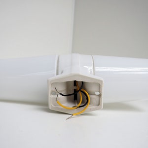 May include: White ceramic wall sconce with two light fixtures and exposed wiring. The sconce has a simple, modern design.