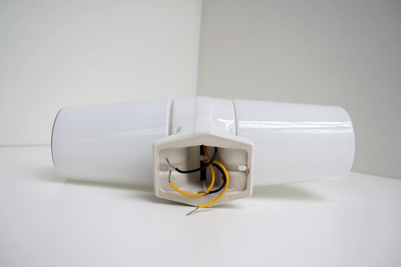 May include: White ceramic wall sconce with two light fixtures and exposed wiring. The sconce has a simple, modern design.