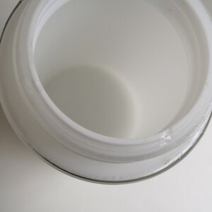 May include: White glass jar with a wide opening and a smooth, rounded rim. The jar is empty and appears to be made of frosted glass.