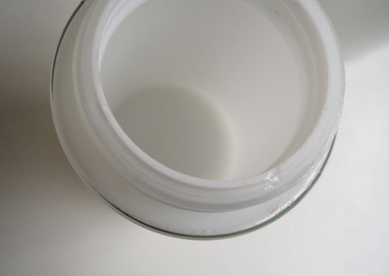 May include: White glass jar with a wide opening and a smooth, rounded rim. The jar is empty and appears to be made of frosted glass.