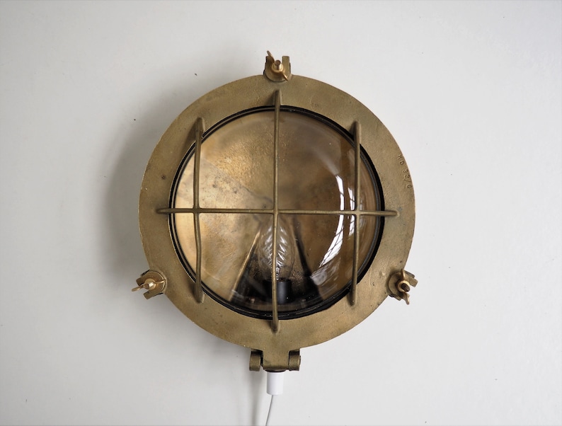 May include: A brass nautical wall light with a round, clear glass lens and a wire cage. The light has a cord and plug.