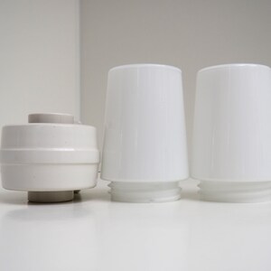 May include: Three white ceramic lampshades, two are tall and cylindrical, one is shorter and round.