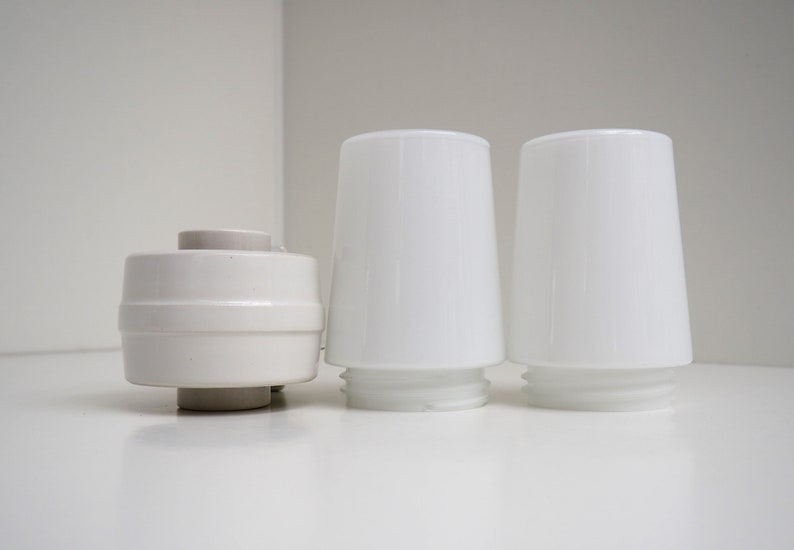May include: Three white ceramic lampshades, two are tall and cylindrical, one is shorter and round.