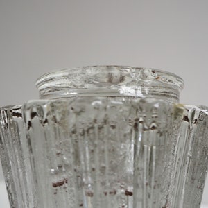 May include: Clear glass vase with a textured, ribbed design. The vase has a wide, open top and a narrow base.