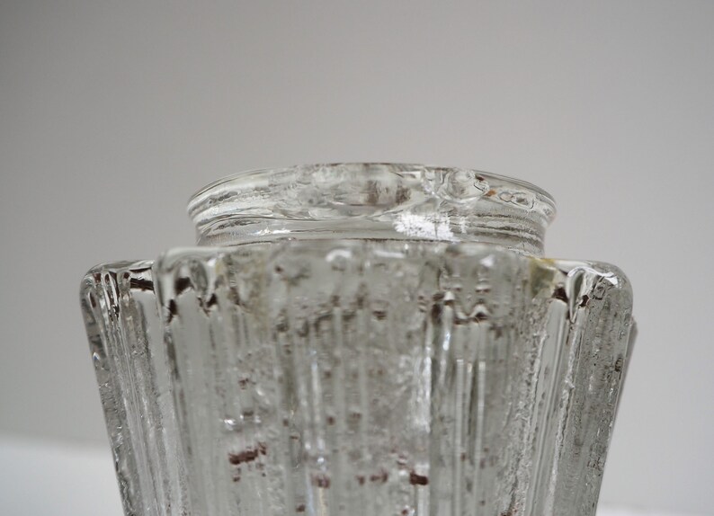 May include: Clear glass vase with a textured, ribbed design. The vase has a wide, open top and a narrow base.