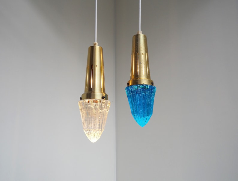 May include: Two gold pendant lights with clear and blue glass shades. The shades are textured and have a pointed shape.