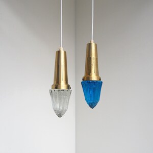 May include: Two hanging pendant lights with brass fixtures and glass shades. One shade is clear glass and the other is blue.