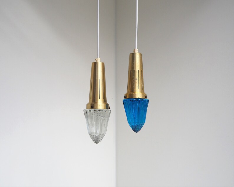 May include: Two hanging pendant lights with brass fixtures and glass shades. One shade is clear glass and the other is blue.