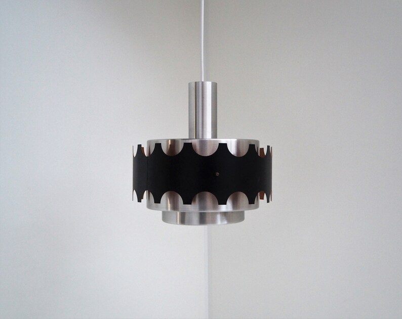 May include: A silver and black pendant light with a scalloped edge. The light is hanging from a white cord.