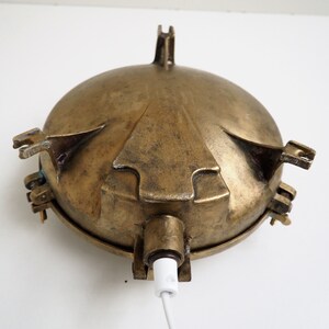 May include: A brass nautical wall light with a round, domed shade and a white cord. The light has four decorative arms that extend from the shade.