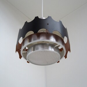 May include: A modern, mid-century style pendant light fixture with a black, copper, and silver finish. The light has a circular, geometric design with a perforated metal shade.