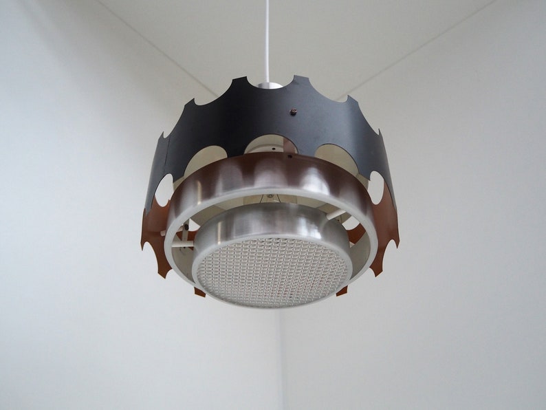 May include: A modern, mid-century style pendant light fixture with a black, copper, and silver finish. The light has a circular, geometric design with a perforated metal shade.