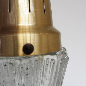 May include: Close-up of a gold metal lampshade with a textured glass base. The lampshade has a small hole in the center.