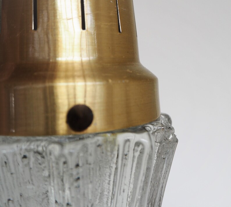 May include: Close-up of a gold metal lampshade with a textured glass base. The lampshade has a small hole in the center.