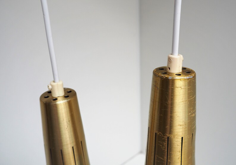 May include: Two gold-toned metal pendant lights with white cords hanging from the ceiling. The lights have a cylindrical shape with a textured surface and a series of small holes around the top.