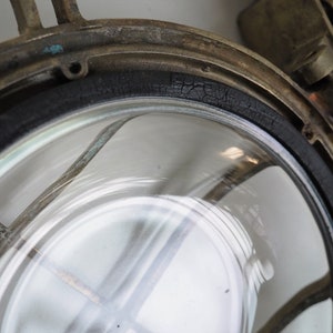 May include: Close-up of a brass nautical light fitting with a cracked black rubber gasket around the glass lens.