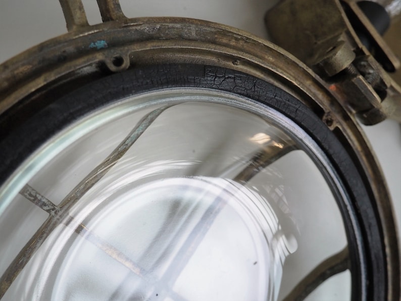 May include: Close-up of a brass nautical light fitting with a cracked black rubber gasket around the glass lens.