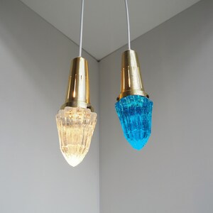 May include: Two pendant lights with gold metal fixtures and glass shades. One shade is clear and the other is a vibrant blue.