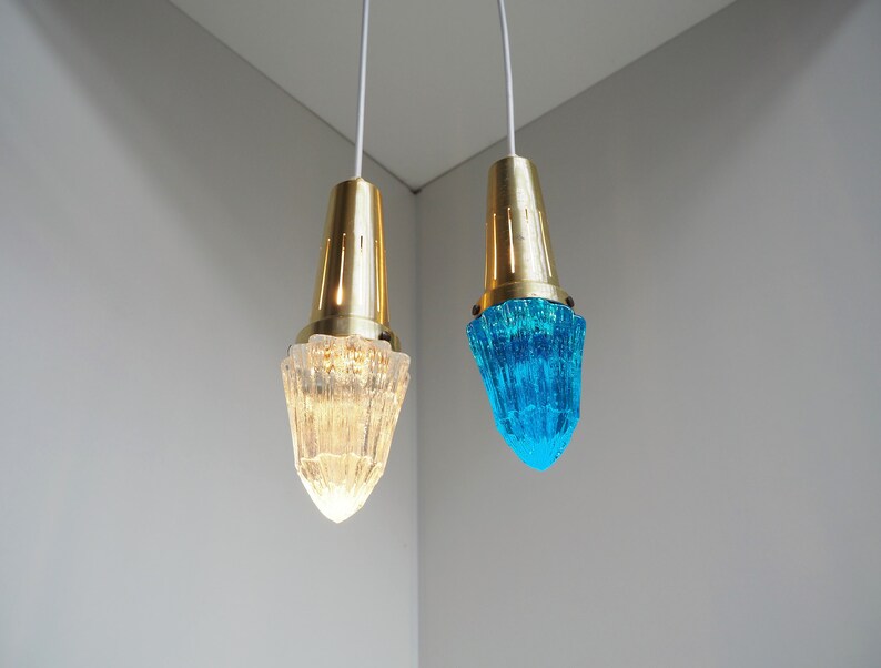 May include: Two pendant lights with gold metal fixtures and glass shades. One shade is clear and the other is a vibrant blue.
