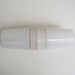 May include: A white ceramic cylindrical container with a decorative band around the middle.