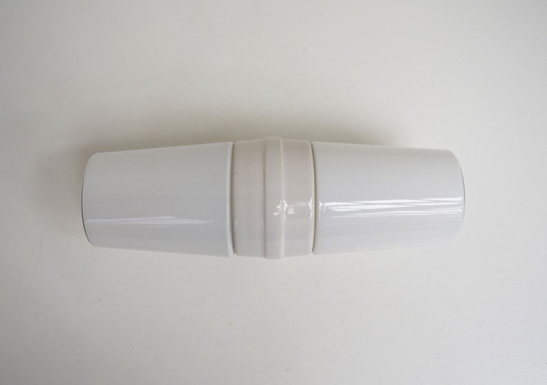 May include: A white ceramic cylindrical container with a decorative band around the middle.