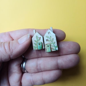 Op de afbeelding: Twee kleine witte keramische huisjes met groene details en een groene deur. De huisjes staan op een hand.