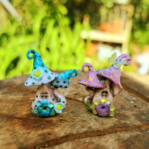 May include: Two whimsical mushroom-shaped figurines with colourful polka dot hats and decorative details. One is blue and green with a white flower, the other is pink and purple with a butterfly.