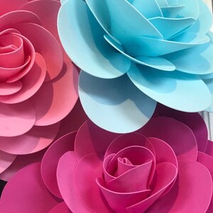 May include: Three large paper flowers in pink, blue, and hot pink. The flowers are made of multiple layers of paper, creating a 3D effect.