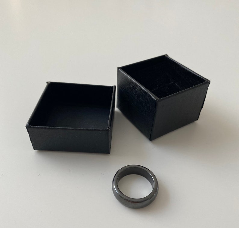 May include: A black ring made of hematite in a black ring box. The ring is smooth and has a polished finish.