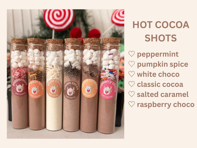 Może przedstawiać: Sześć szklanych prob&oacute;wek wypełnionych warstwową mieszanką do gorącej czekolady i zwieńczonych miniaturowymi białymi piankami marshmallow. Każda prob&oacute;wka posiada okrągłą etykietę z napisem: peppermint, pumpkin spice, white choco, classic cocoa, salted caramel, raspberry choco.