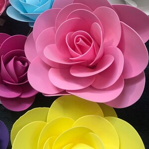 May include: A collection of paper flowers in various colours, including pink, blue, yellow, and white. The flowers are layered and have a 3D effect.