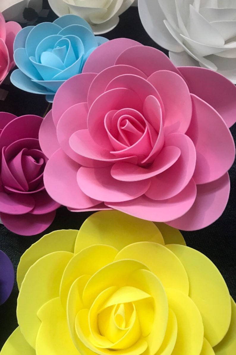 May include: A collection of paper flowers in various colours, including pink, blue, yellow, and white. The flowers are layered and have a 3D effect.