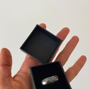 May include: A silver ring in a black ring box. The box is open and the ring is visible.