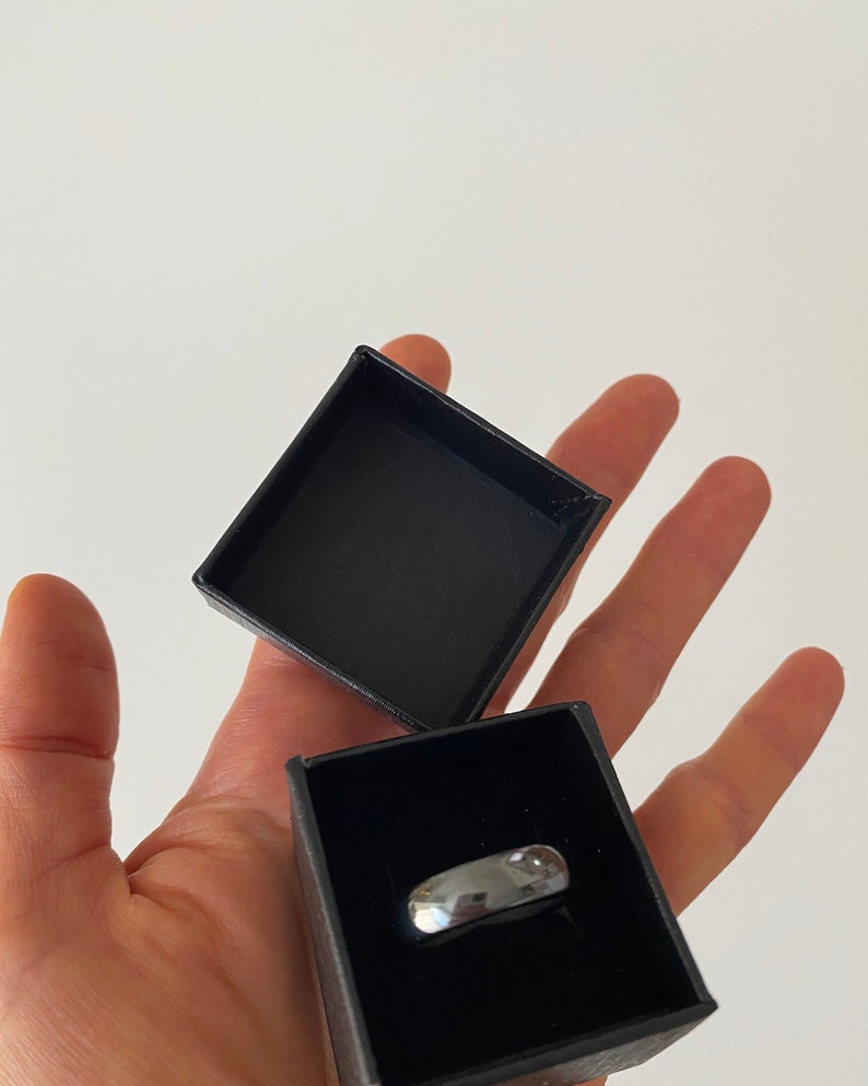 May include: A silver ring in a black ring box. The box is open and the ring is visible.