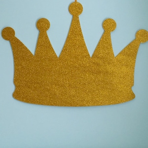 May include: A gold glitter crown with a pointed top and five points. The crown is a decorative item.