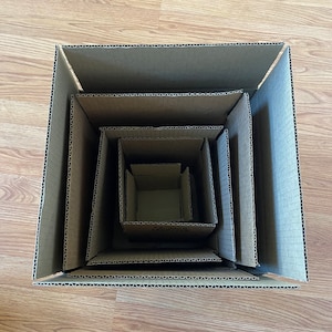 May include: A set of five nested cardboard boxes, each slightly smaller than the one before it. The boxes are all made of brown cardboard and have a corrugated texture.