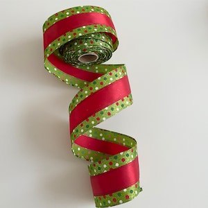 May include: A roll of decorative ribbon with a festive design. The ribbon features alternating sections of solid red and green with white and red polka dots. The ribbon is made of a shiny material and is ideal for holiday crafts and gift wrapping.