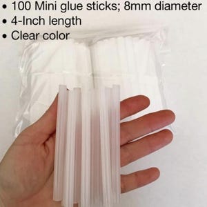 Może przedstawiać: Przezroczyste mini sztyfty kleju. Obraz przedstawia opakowanie 100 sztyftów kleju, każdy o średnicy 8 mm i długości 10,16 cm. Sztyfty kleju są przezroczyste.