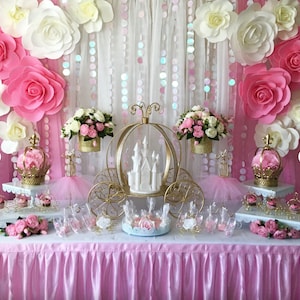 May include: A pink and white princess themed party dessert table with a gold carriage centrepiece, white cake, pink and white flowers, and cupcakes.