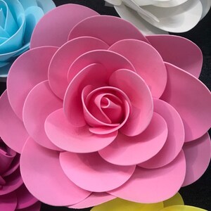 May include: A large pink paper flower with multiple layers of petals. The flower is made of paper and has a delicate, layered design.