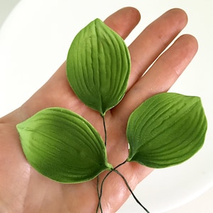 May include: Four green leaves with a veined texture, wired together for crafting or decorating.