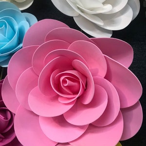 May include: A large, pink paper flower with multiple layers of petals. The flower is made of paper and has a delicate, layered design.