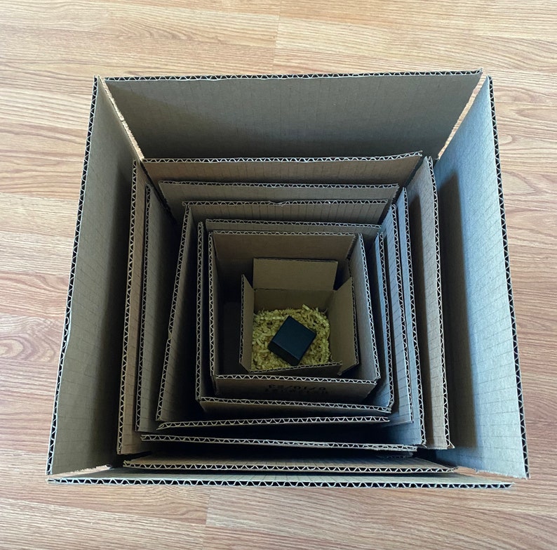 May include: A brown cardboard box with multiple layers, each slightly smaller than the one before it. The box is empty except for a small black square object in the center.
