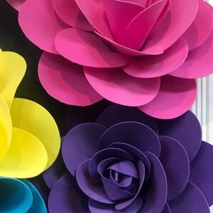 May include: Three large paper flowers in shades of pink, purple, and yellow. The flowers are layered and have a 3D effect.