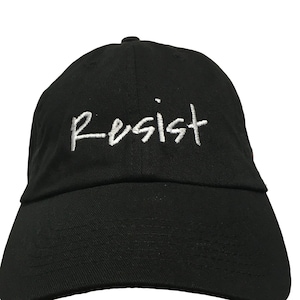 May include: A black baseball cap with a white embroidered word "Resist" on the front.
